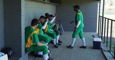 Diverse cricket teammates in dugout celebrating high five camaraderie green-yellow uniforms