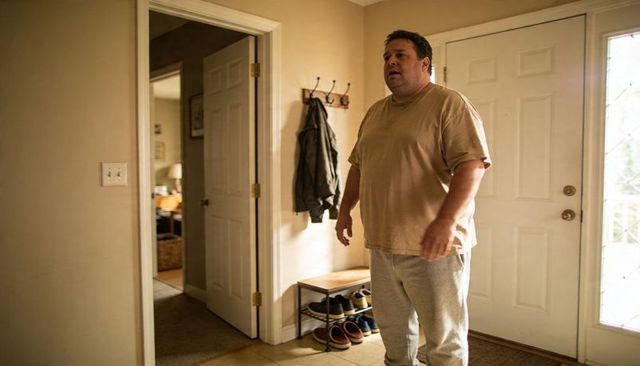 Casual man arriving home standing in sunlit foyer wearing tan shirt and sweatpants