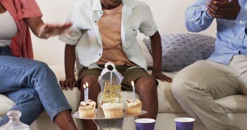 African American Family Celebrating Child Birthday on Sofa with Cupcakes and Lit Candles