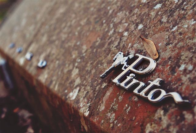Image depicting the close-up of a weathered Pinto car emblem on a rusty surface showcasing the age and patina of a vintage vehicle. Excellent for use in automotive history articles, advertisements for car restoration services, or as a visual presentation of vintage car aesthetics.