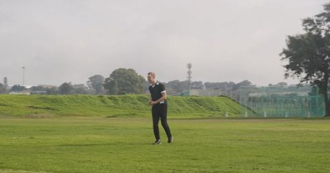 Man strolling lawn of suburban park on cloudy day