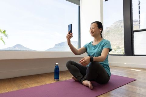 Mature asian woman practicing yoga at home, smiling during virtual class with phone