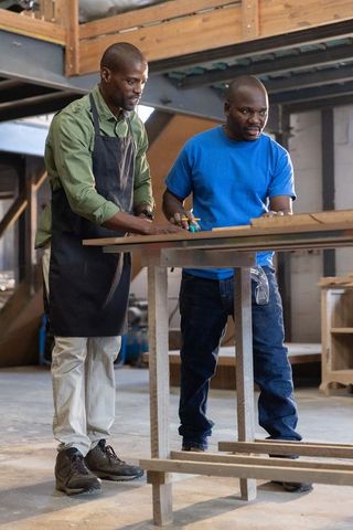 African american carpenters measuring and marking wooden plank on workbench in workshop