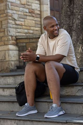 Smiling man sitting on stone steps outside masonry building with backpack and smartwatch