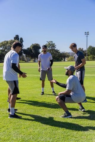 Multicultural men practicing football passing drill on sunlit green park field