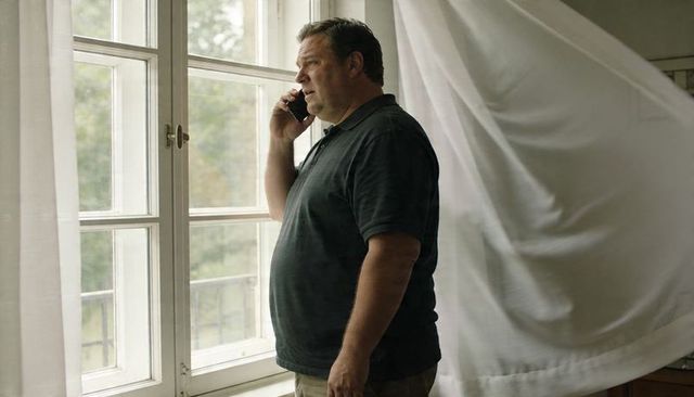 Man standing by window talking on smartphone with billowing curtain and balcony view