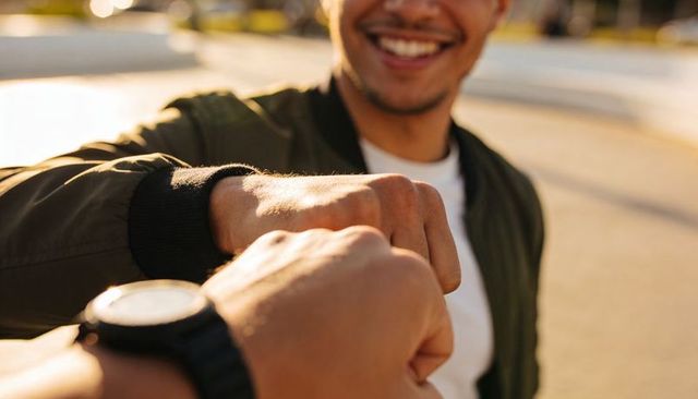 Friends fist-bumping at golden hour, smiling man in jacket, closeup hands showing teamwork