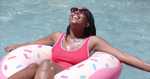 African woman relaxing on pink donut float soaking up sun in sparkling pool summer leisure