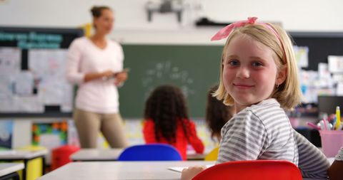 Cheerful Schoolgirl in Classroom with Teacher in Background