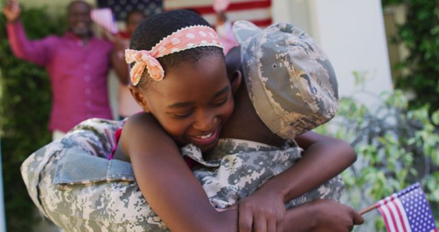 African american soldier father hugging smiling daughter with family and american flag behind. soldier returning home to family. ehind