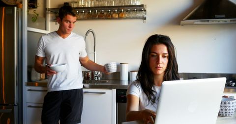 Couple in Kitchen: Woman Working on Laptop, Man Having Coffee