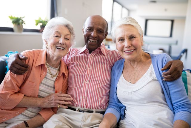 Senior man and two female friends sitting closely on sofa, smiling warmly. Ideal for illustrating themes of companionship, elderly care, retirement living, and community bonding. Suitable for use in healthcare, senior living, and lifestyle publications.