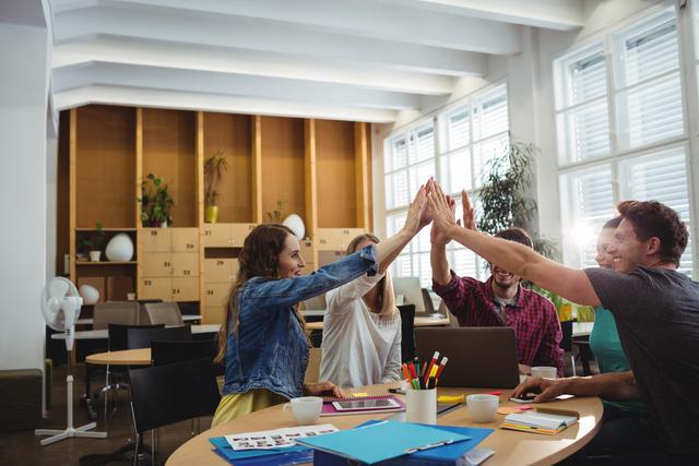 Young professionals in a modern office celebrating success with a high five. Ideal for illustrating teamwork, collaboration, and a positive work environment in business presentations, marketing materials, and corporate websites.