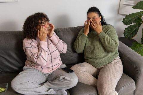 Diverse friends relaxing on couch applying under-eye patches during cozy at-home self-care