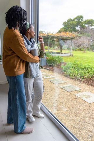African american couple embracing by glass door looking out over garden with pergola