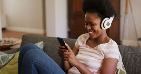 Woman Relaxing on Couch Wearing Headphones and Smiling at Phone