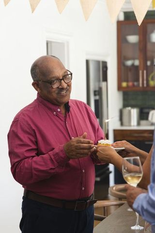 Senior african american man receiving dessert with lit candle celebrating birthday at home