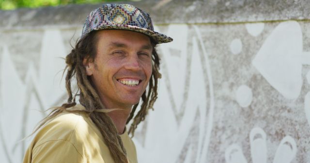 Image portrait of smiling caucasian male artist with dreadlocks painting mural on wall. Freedom, creativity, inclusivity and hobbies concept digitally generated image.