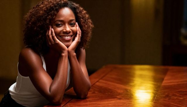 Smiling woman leaning on reflective dining table under warm ambient light, cozy portrait