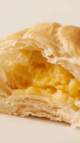 Vertical closeup video showing bitten flaky pastry revealing creamy custard filling and glossy glaze