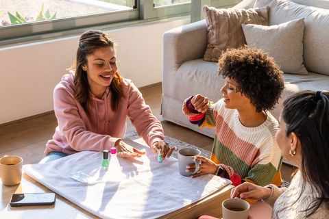 Sunlit at-home manicure among multiracial friends sharing coffee and cozy conversation