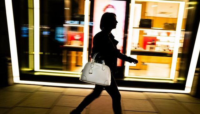 Silhouette woman walking past illuminated boutique window carrying white handbag at night