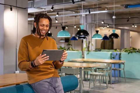 African American man smiling using tablet in modern coworking lounge with teal lighting