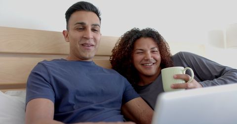 Happy Gay Couple Using Laptop and Drinking Coffee in Bed