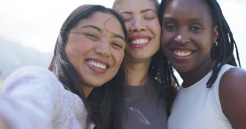 Smiling diverse friends taking selfie outdoors on sunny day