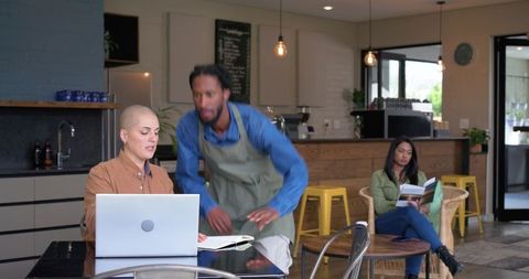 Barista rushing past customer working on laptop in modern cafe coworking scene