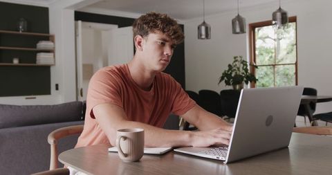 Young Man Working Remotely at Dining Table with Laptop and Coffee Minimal Contemporary Home