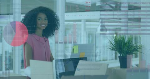 Smiling analyst standing at workstation with laptop, charts and glass data overlays