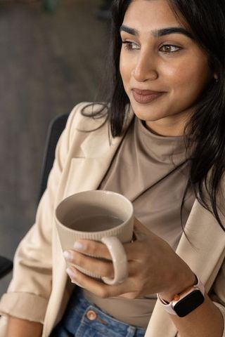 Indian business woman holding mug in beige blazer relaxed three-quarter office portrait