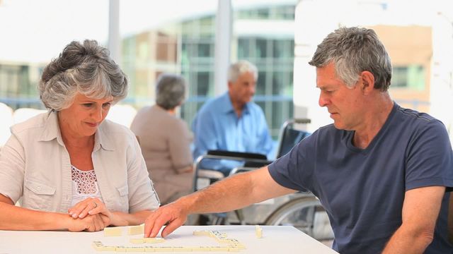 Senior couple enjoying a game of dominoes at a table, suggesting leisure time during retirement. Could be used in advertisements or articles about retirement communities, elderly activities, or promoting mental engagement among seniors.