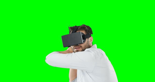 Man wearing VR headset experiencing virtual reality against green screen background. Ideal for technology demonstrations, virtual reality experiences, software advertisements, and innovative tech promotions.