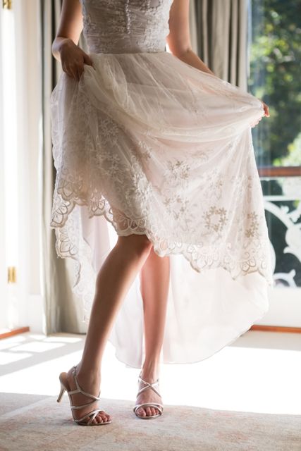 Low section of bride in wedding dress and sandals standing on floor at home