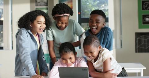 Diverse Elementary Students Laughing and Collaborating Around Tablet in Bright Classroom