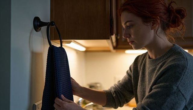 Red-haired woman adjusting navy towel under warm cabinet light in cozy kitchen