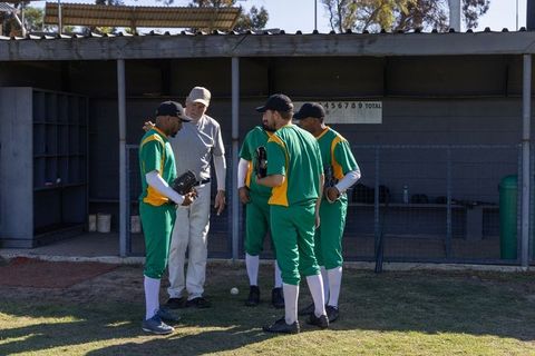 Baseball team huddling with coach by dugout on sunlit community field