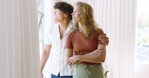 Couple in Sunlit Room Looking Out Window, Embracing Modern Lifestyle