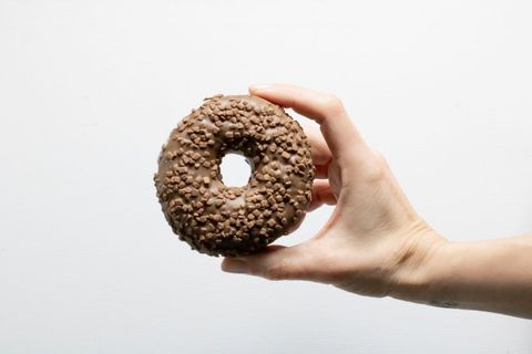 Hand holding chocolate donut with nuts against white background