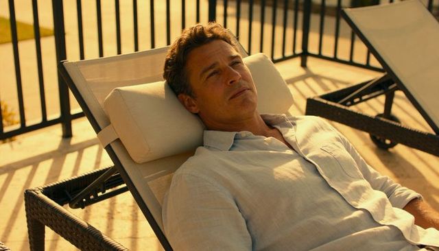 Relaxing man reclining on sunlit wicker lounger with linen shirt and patio railing shadows