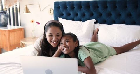 Asian Mother and Daughter Relaxing on Bed with Laptop