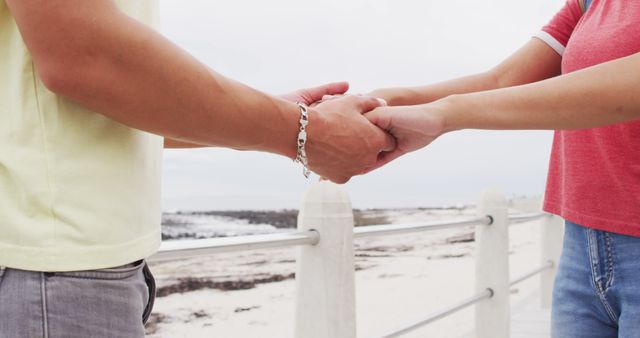 Two people holding hands by beachside promenade, wearing casual clothing. Perfect for themes of relationship, love, summer vacation, and serene moments by the seaside.