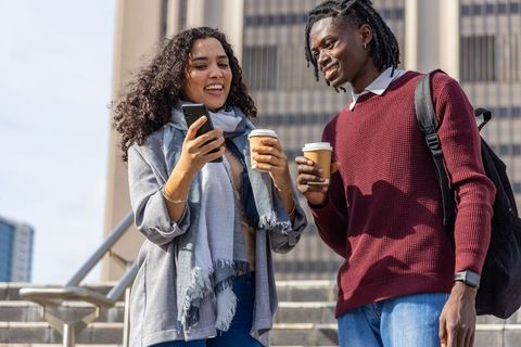 Students sharing coffee and smartphone on urban campus stairs