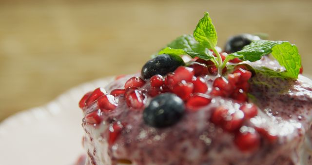 A close-up view of a dessert topped with fresh blueberries, pomegranate seeds, and a sprig of mint, with copy space. Its vibrant colors and presentation suggest a focus on both taste and visual appeal.