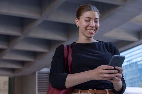 Young african american woman smiling and checking smartphone under modern concrete canopy