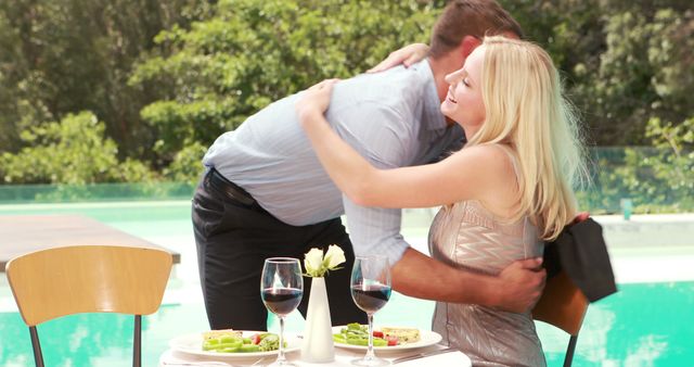 A Caucasian couple enjoys a romantic embrace by a poolside dining table, with copy space. Their affectionate moment adds a touch of intimacy to the outdoor setting.
