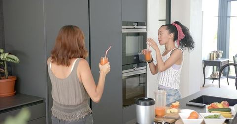 Two Young Women Enjoying Fresh Juice in Modern Kitchen