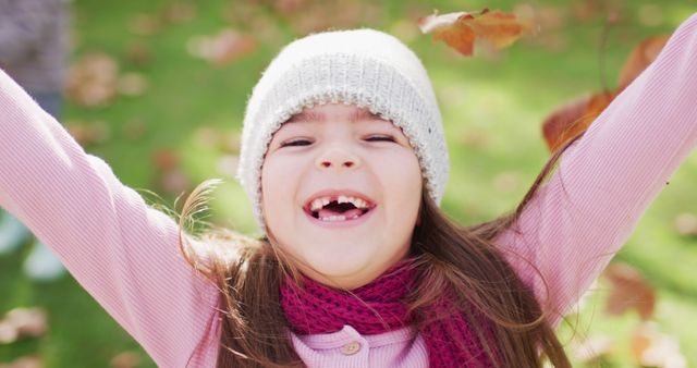 Image of happy caucasian girl in woolly hat and scarf throwing autumn leaves in garden. Childhood, health and happiness concept digitally generated image.